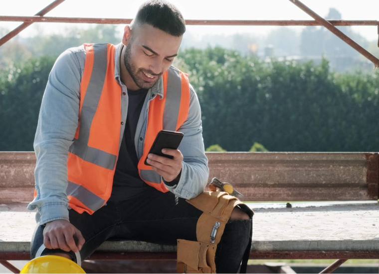 Site worker in hi-vis using the Assignar app on a phone
