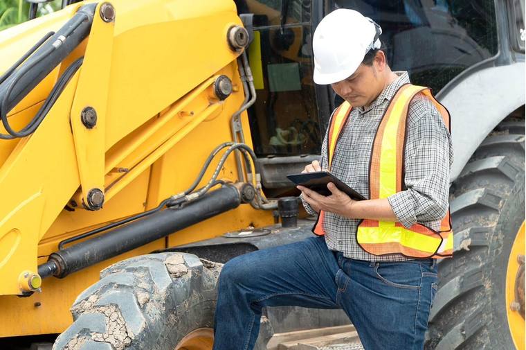 Site supervisor reviewing allocations on a tablet beside an excavator